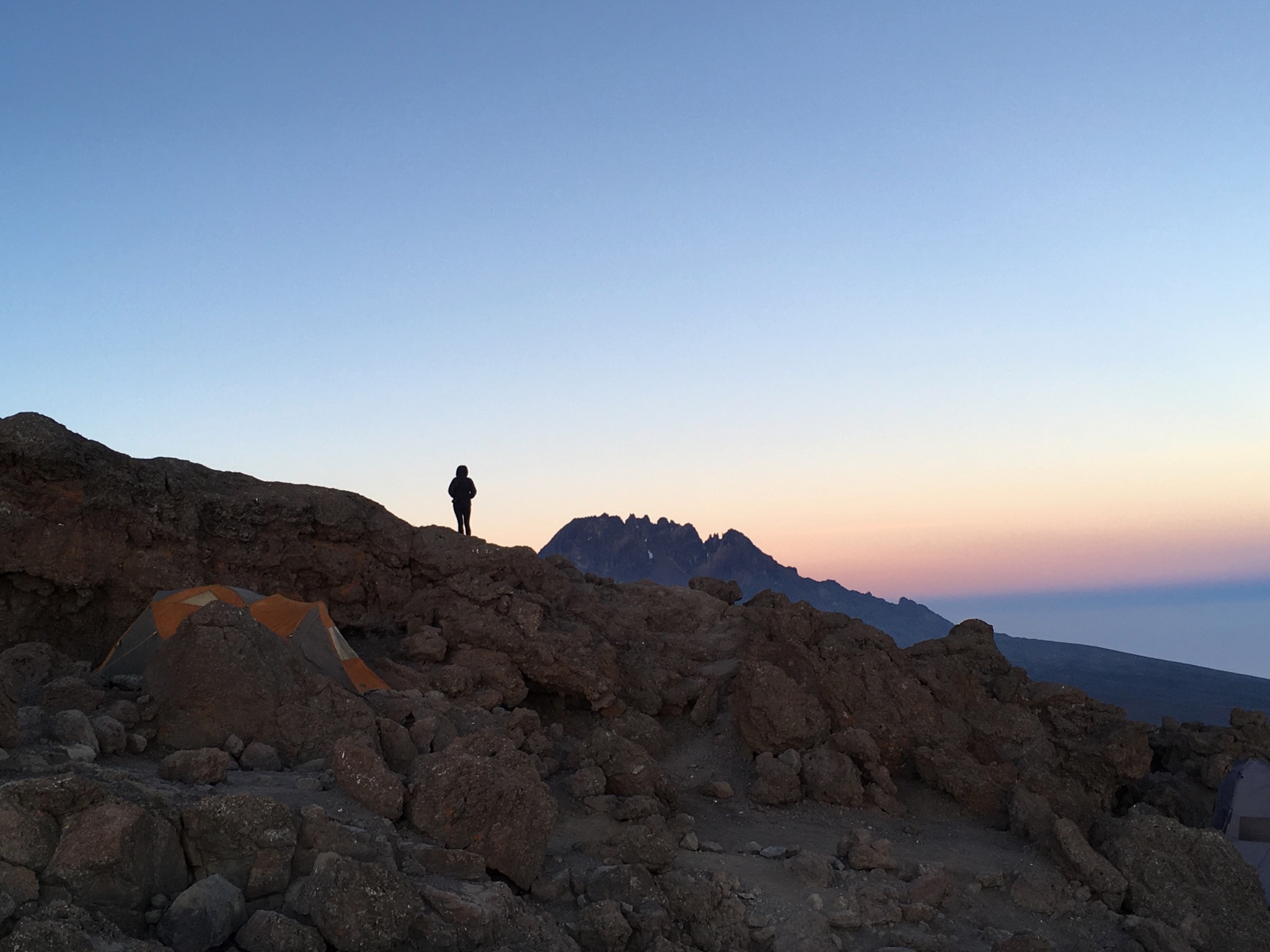 Photo of a person standing on a mountain ridge overlooking sunset. Photo by the author.